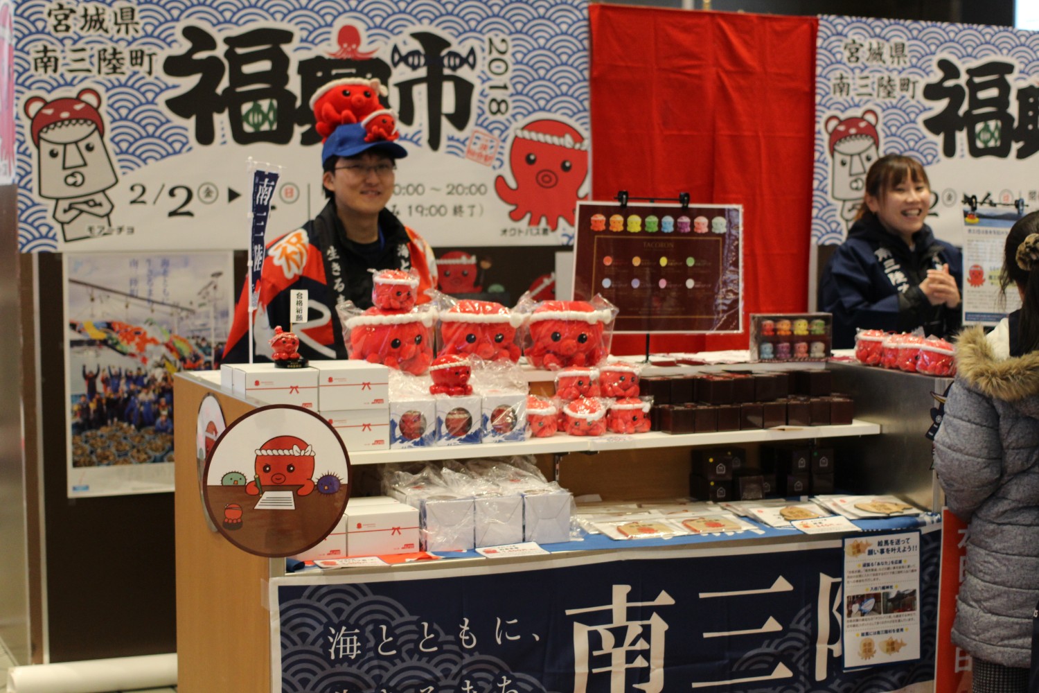 福興市の店舗でオクトパス君をモチーフにしたキャラクターグッズが多数並び、男性と女性のスタッフが笑顔で接客している様子の写真