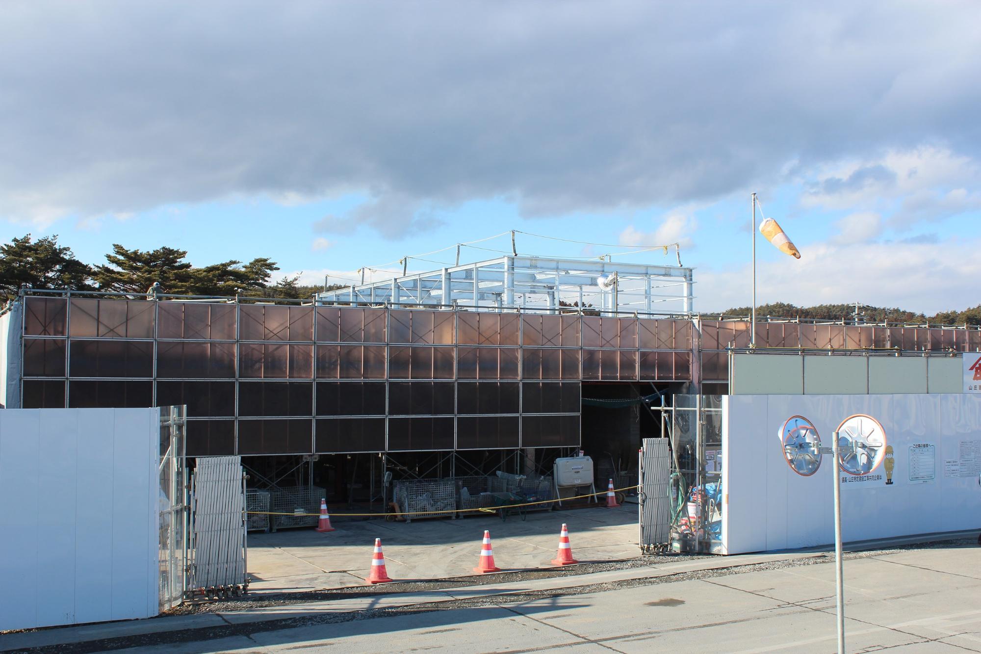 建物の外壁の足場が整い、屋上部分に金属の構造体が現れた工事中盤の建設現場の写真