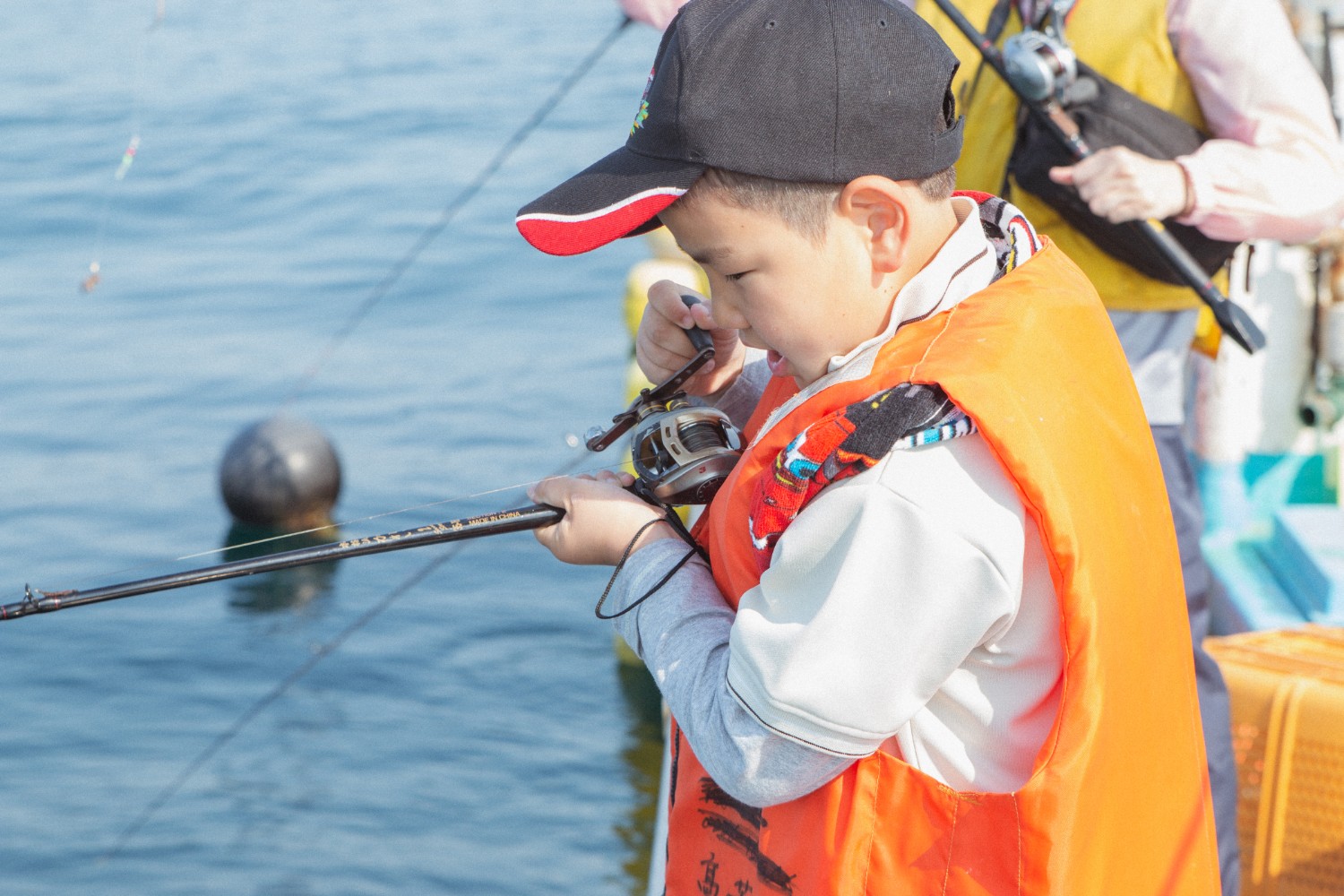 黒いキャップを被った芳雅くんが、釣り竿のリール部分を見ながら集中して引き上げている様子の写真