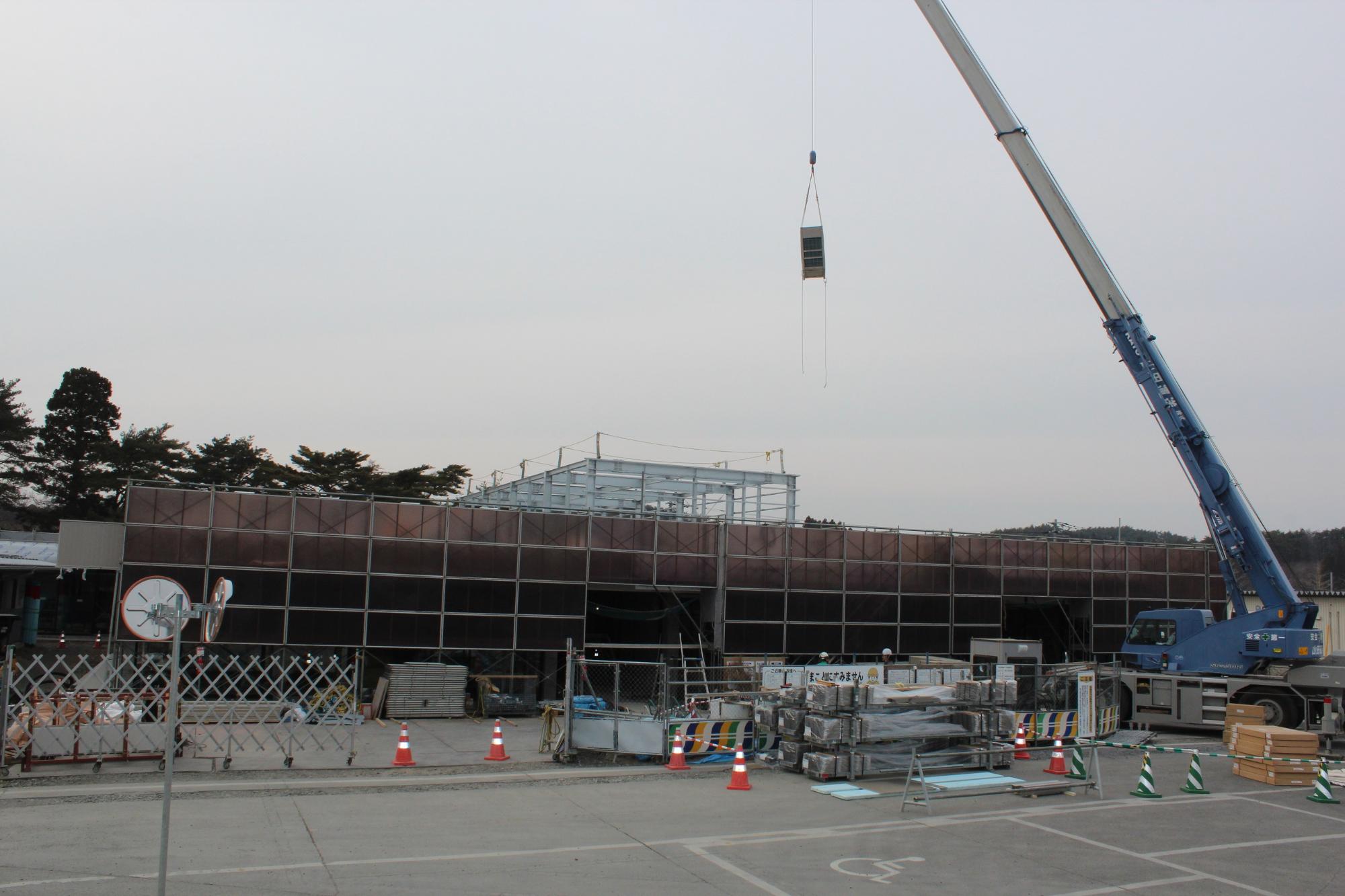 大きなクレーンで建材を持ち上げる様子が写され、建物の骨組みと外装工事が進む建設現場の写真