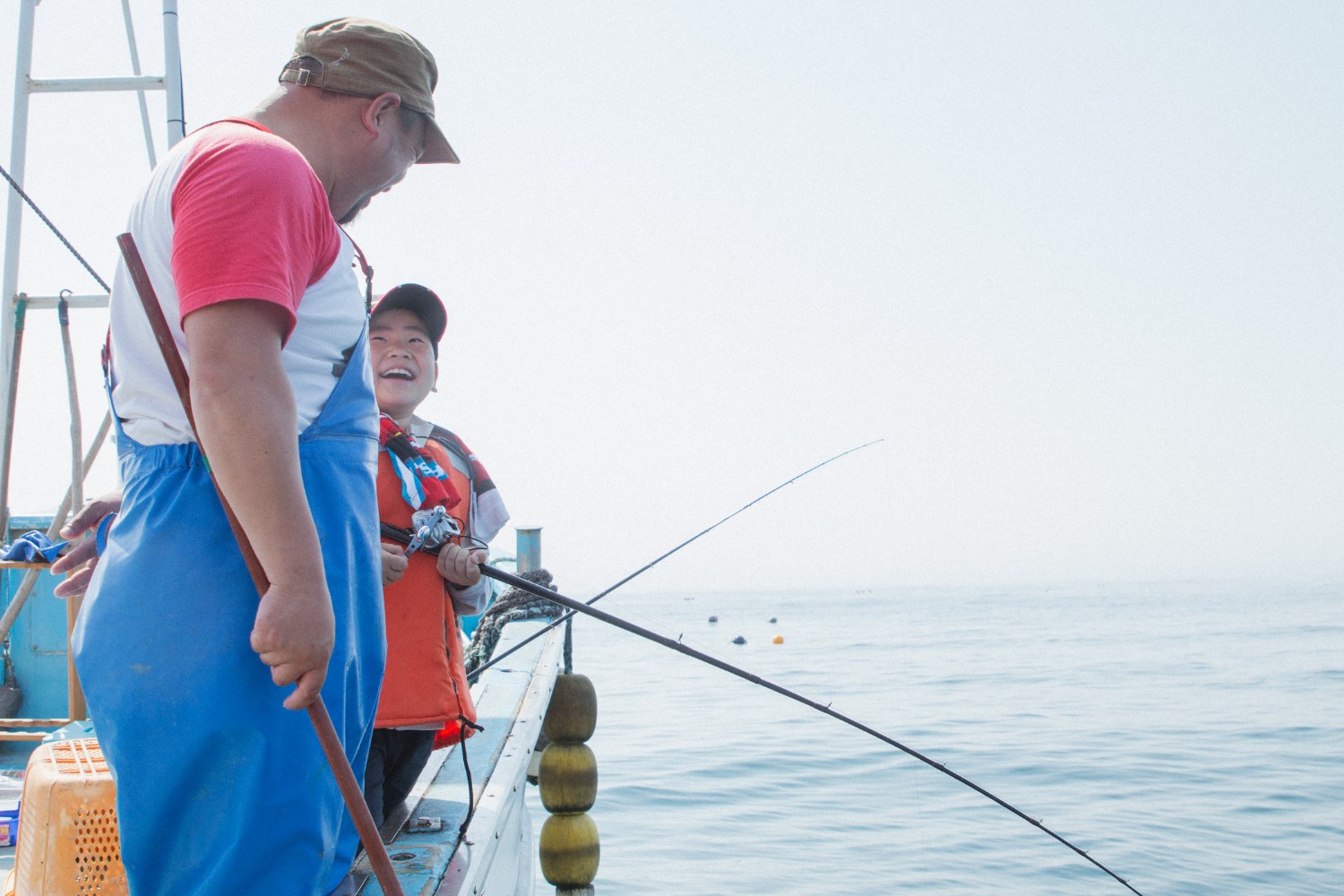 釣り船の上で父親と芳雅くんが釣り竿を持って嬉しそうに釣りを楽しんでいる様子の写真