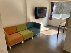 カラフルなソファと壁掛けテレビが設置され、窓から自然光が差し込む明るい休憩スペースの写真