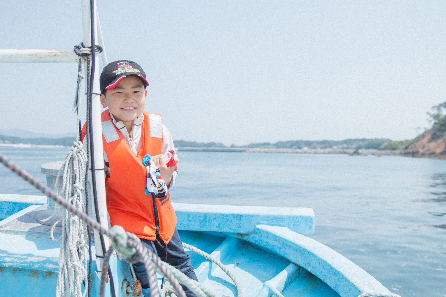 青い船の上でオレンジ色のライフジャケットを着た芳雅くんが笑顔でカメラを見ている写真