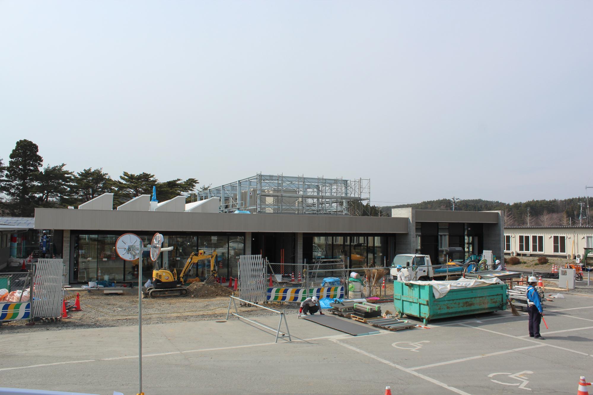 建物の外観がほぼ整い、ガラスの外壁や出入口が完成に近づく建設終盤の写真