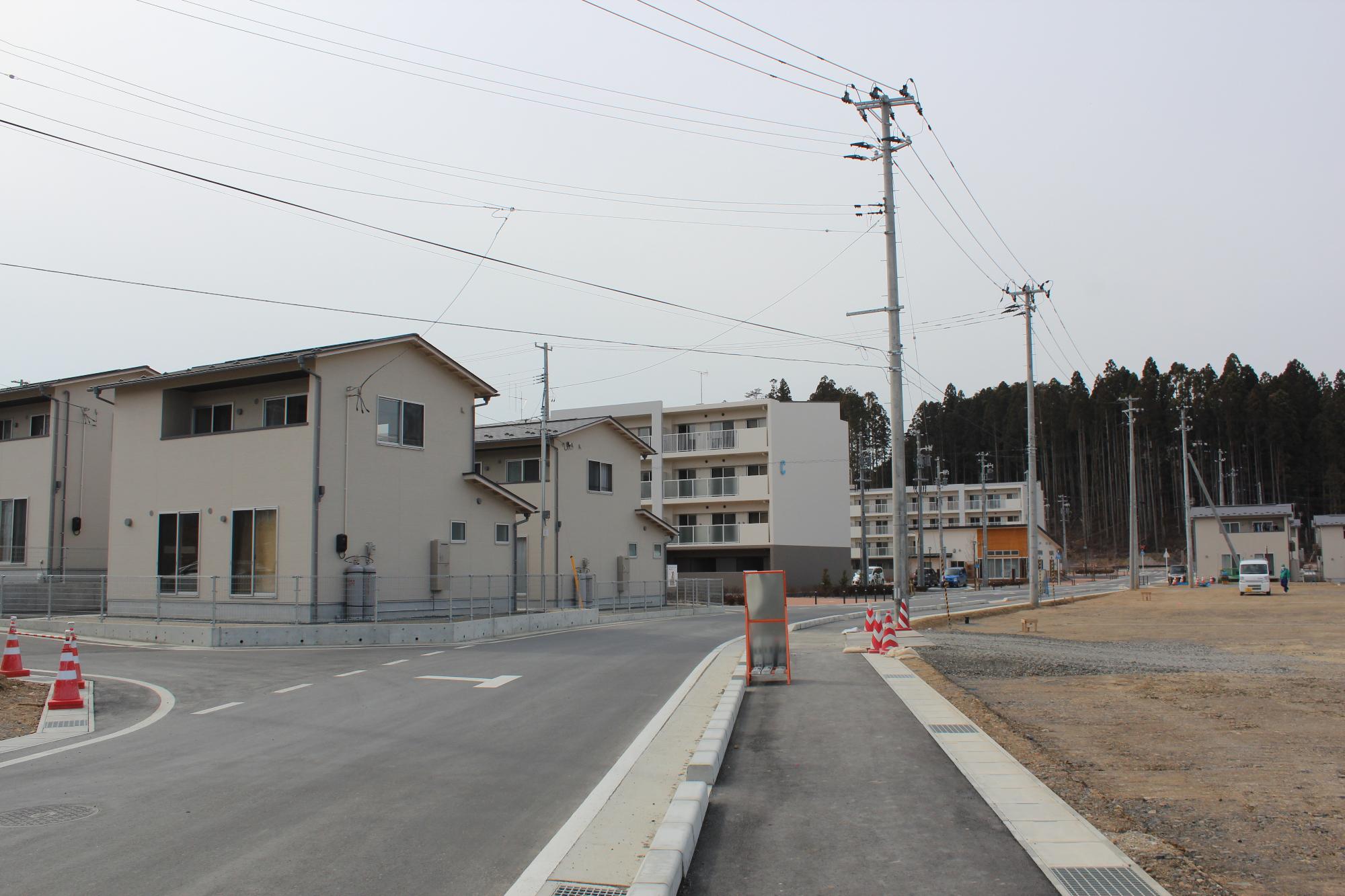 全体が完成した災害公営志津川中央住宅の建物群が整然と並び、舗装された道路や植栽が施された歩道、街灯や防犯カメラも設置され、周囲には新たな生活環境が整った様子が広がっている写真