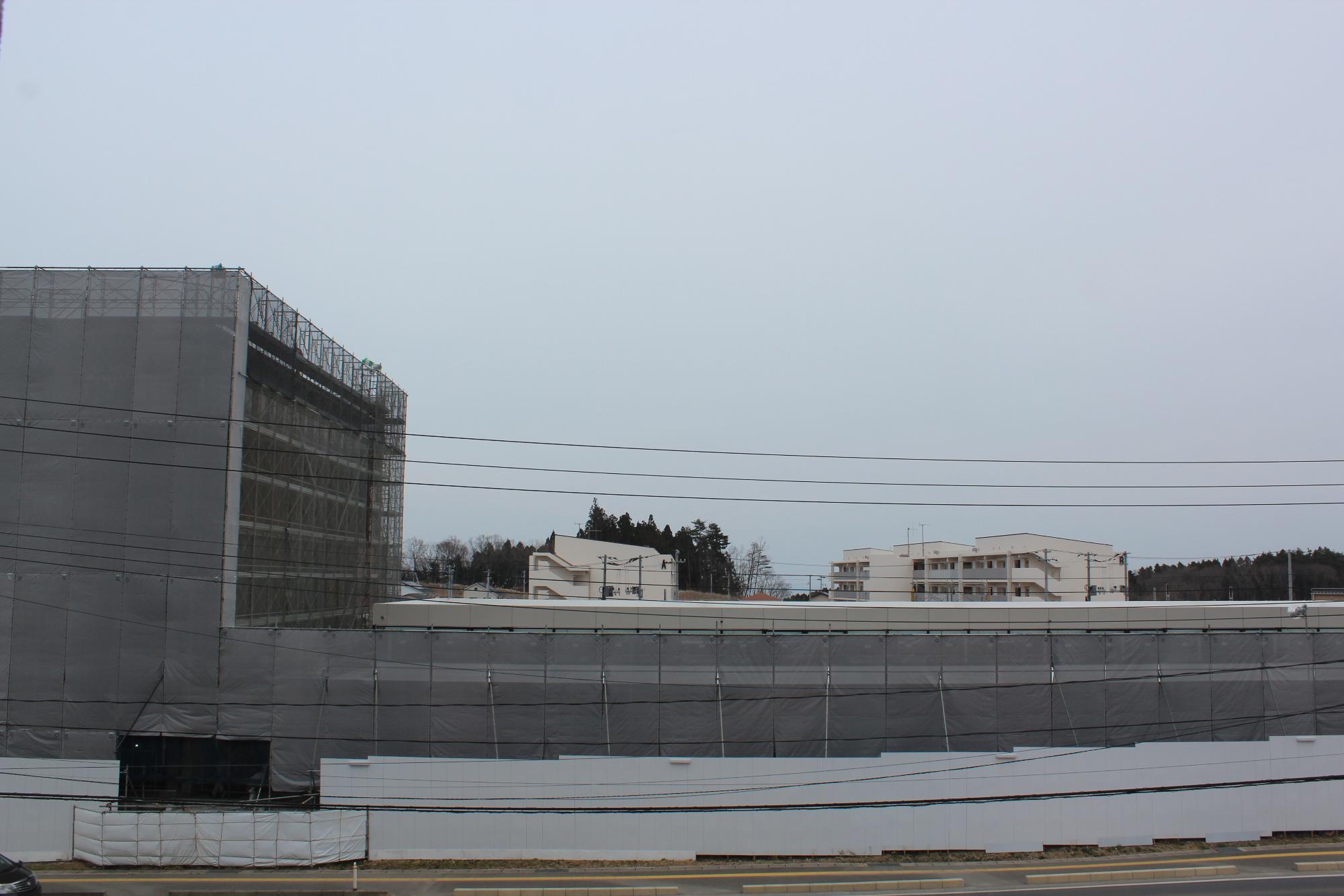 仮設フェンスで建てられた工事現場の中で灰色の防護ネットに覆われた建設中の建物がみえる平成29年4月6日現在の写真