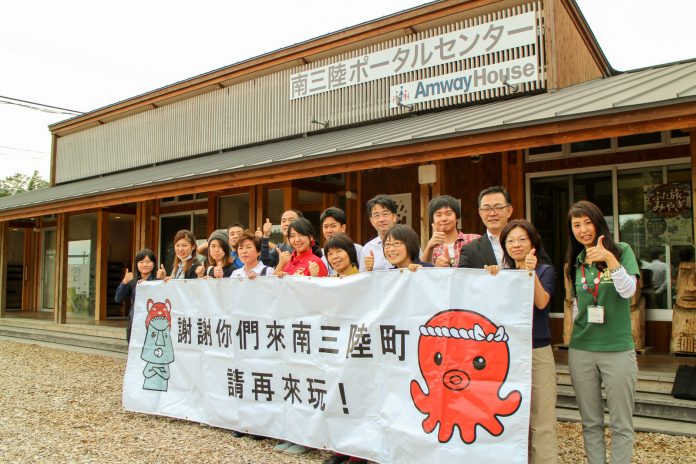 南三陸ポータルセンターの看板が掲げられた建物の前で、オクトパス君のイラストと中国語の文字が書かれた横断幕を手に持ってたくさんの人が並んでいる集合写真