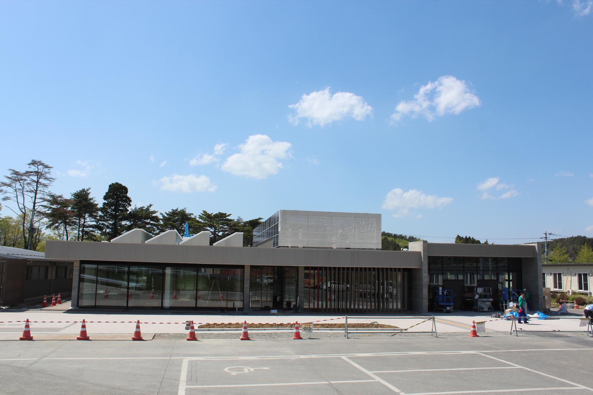 完成間近の施設で、バリアフリー対応の駐車場も確認できる周囲で片付け作業や植栽工事が進む建設最終段階の建設現場の写真