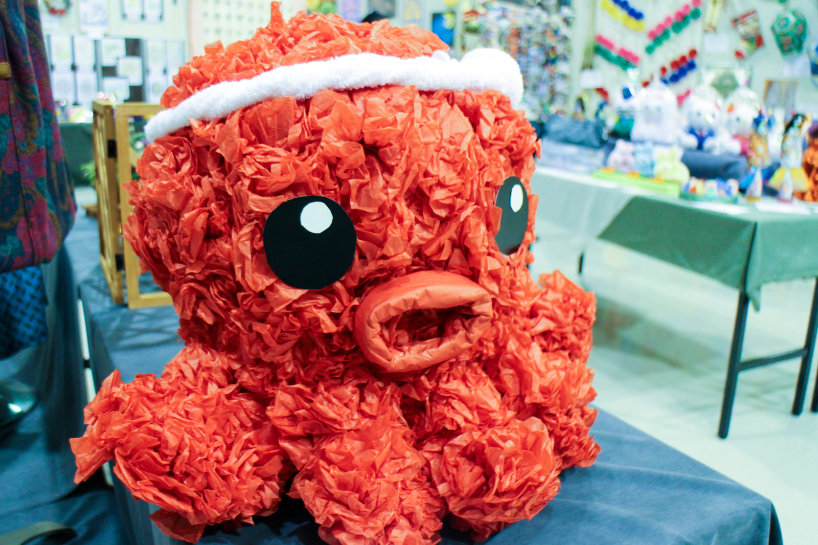 赤い紙をくしゃくしゃにして作られたオクトパス君の大きな装飾がテーブルに置かれている様子を写した、クラフト作品展示の写真