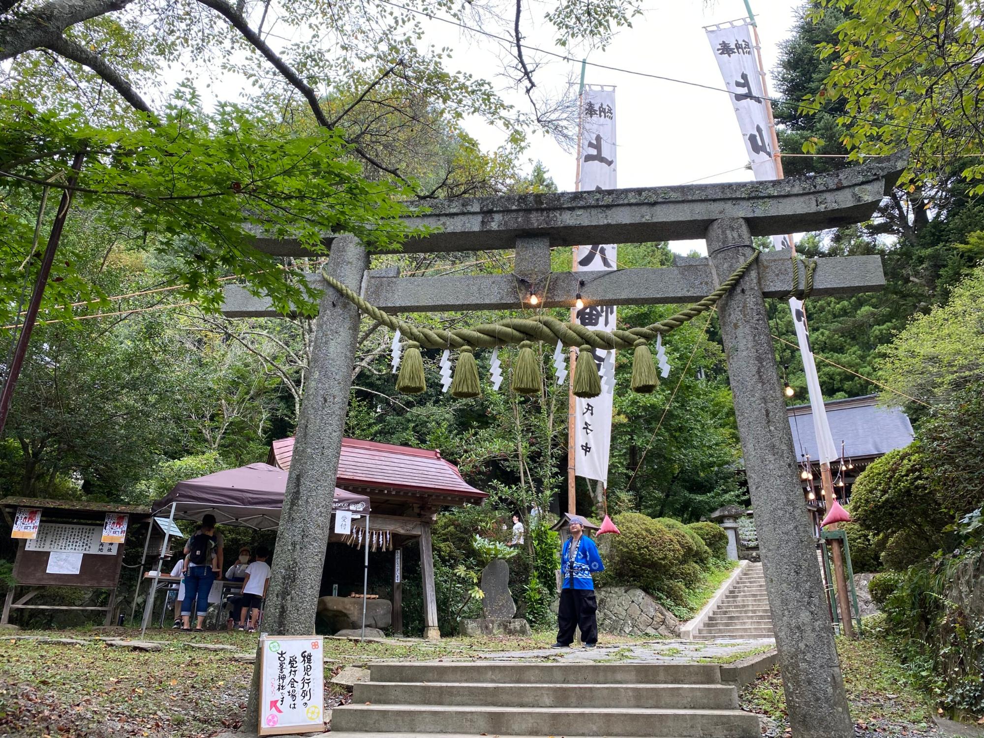 石造りの鳥居の奥に、緑豊かな木々と参道の階段が続く神社の写真