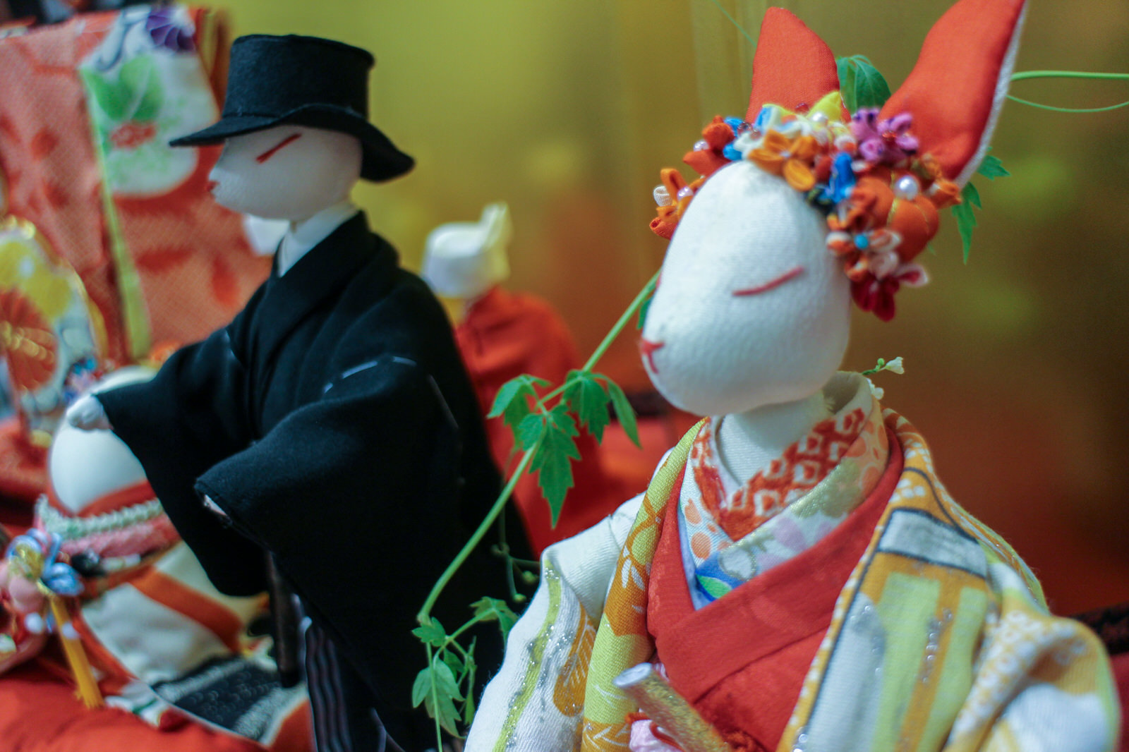 花飾りを頭に載せて目を閉じている色鮮やかな着物を着たウサギの顔をした花嫁人形と、隣には黒い和装と帽子をかぶったもう一体のウサギの人形が並んでいる様子をアップで撮影した写真