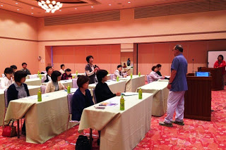 明るい会場で、参加者の一人が医師に質問をしており、他の参加者も着席して真剣に話を聞いているセミナーの一幕の写真