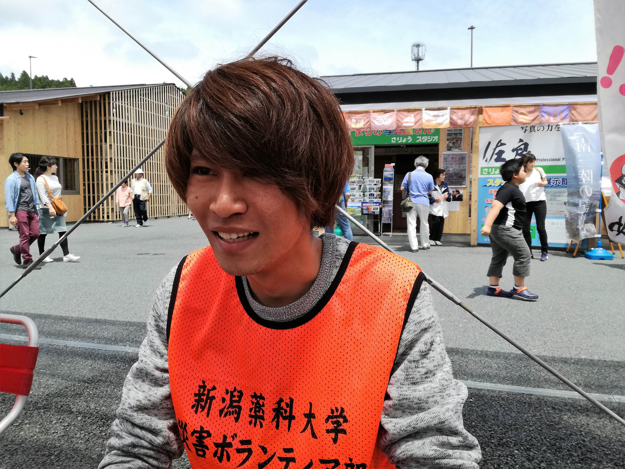 屋外で「新潟薬科大学 災害ボランティア部」のビブスを着た松井智幸さんを写した写真