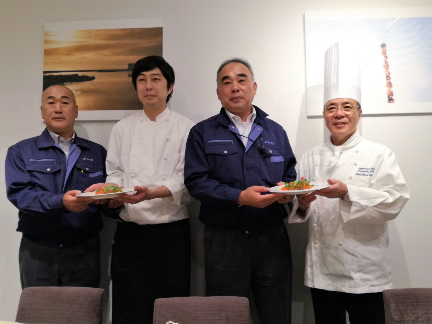 コックコートを着た2人の料理人と2人の漁業関係者が一列に並び、それぞれが手に持った料理皿を正面に見せている写真