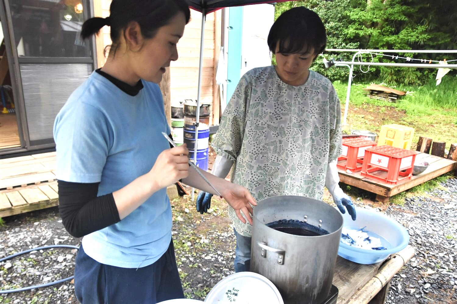 テントの下で女性2人が藍の葉を寸胴鍋で煮出した染料液を作っている写真