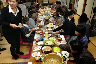 和室に並べられた長い座卓に多くの高齢者が座り、にぎやかに料理を囲んで食事をしている写真