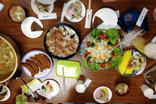 色鮮やかなサラダや煮物、炊き込みご飯、鍋ごと置かれたはっと汁など多種多様な料理が並んでいるテーブルを、上から見下ろす構図で撮影した写真