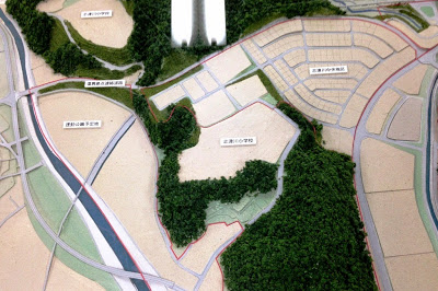 斜面に沿って造成された住宅地と、周囲を取り囲む森林や道路、川が立体的に再現された都市開発の模型の写真