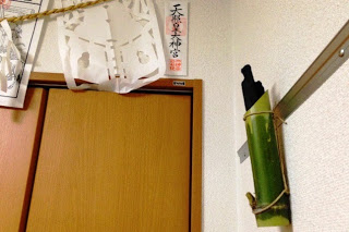 ドアの上の壁に、天照皇大神宮と書かれた神札と、紙垂を垂らした注連縄、さらに竹筒に黒い木炭を差したものが取り付けられている様子を写した、室内に飾られた竹炭の写真