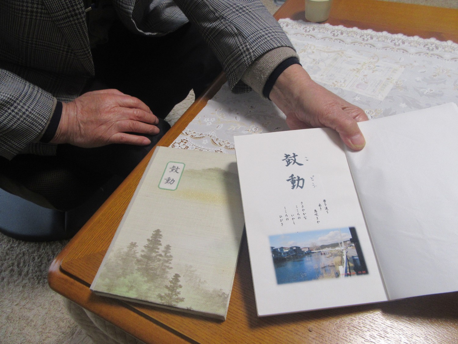 テーブルの上に「鼓動（こどう）」というタイトルの句集の表紙と、男性の手で開いた中身が並べられている写真