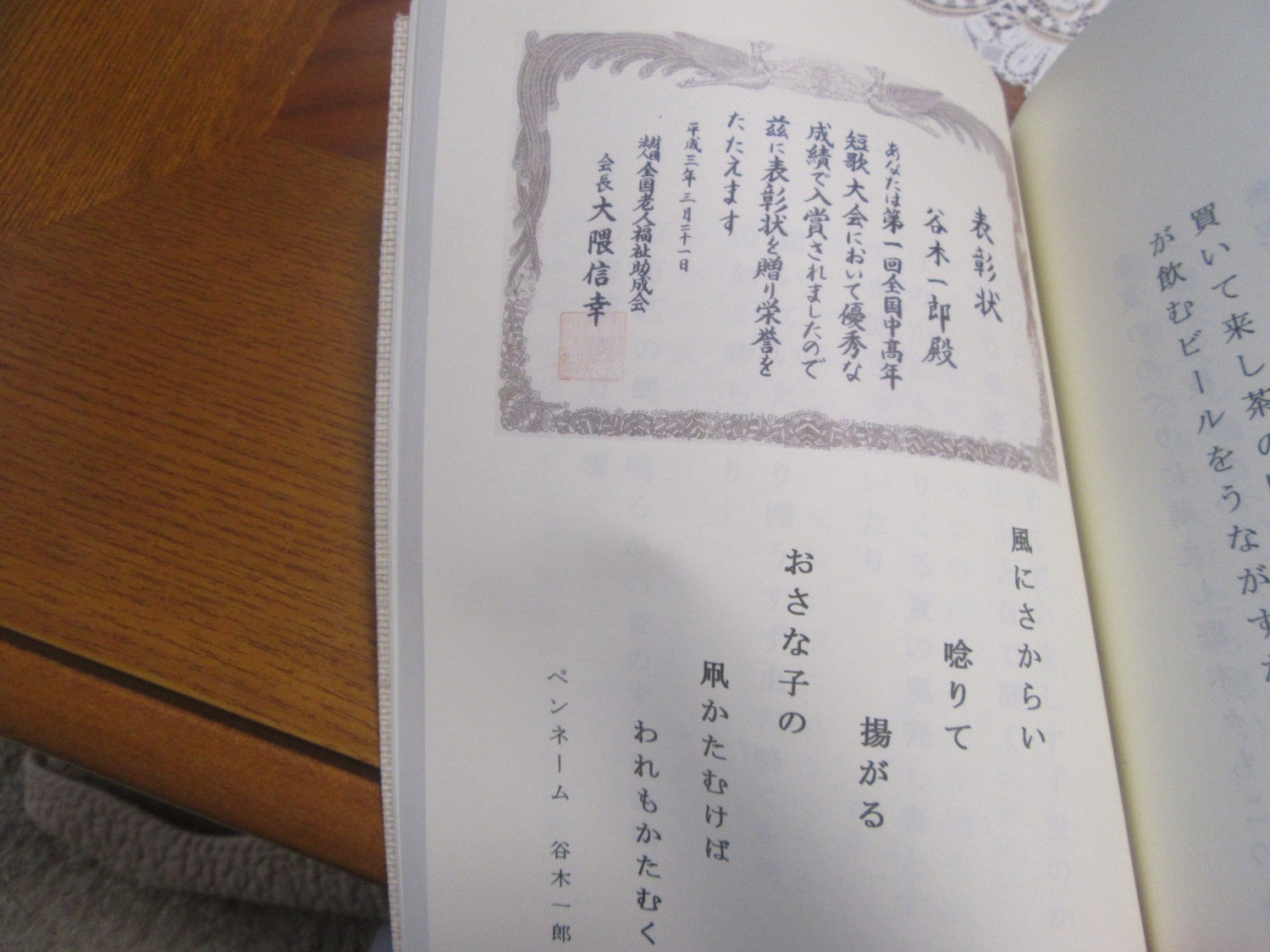 上部に表彰状の写真が載っており、下には短歌が縦書きで記されている、短歌大会で入賞したページを開いた写真