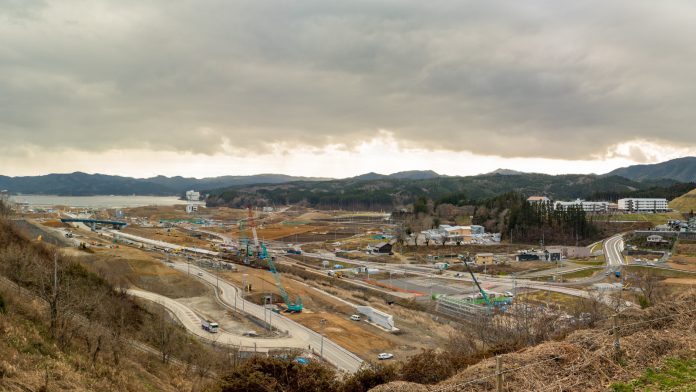 現場には複数のクレーンや建設車両が稼働しており、複数の道路や通路が確認でき背景にはいくつかの建物が見え、周囲は丘や山々に囲まれている大規模な建設現場を写した写真
