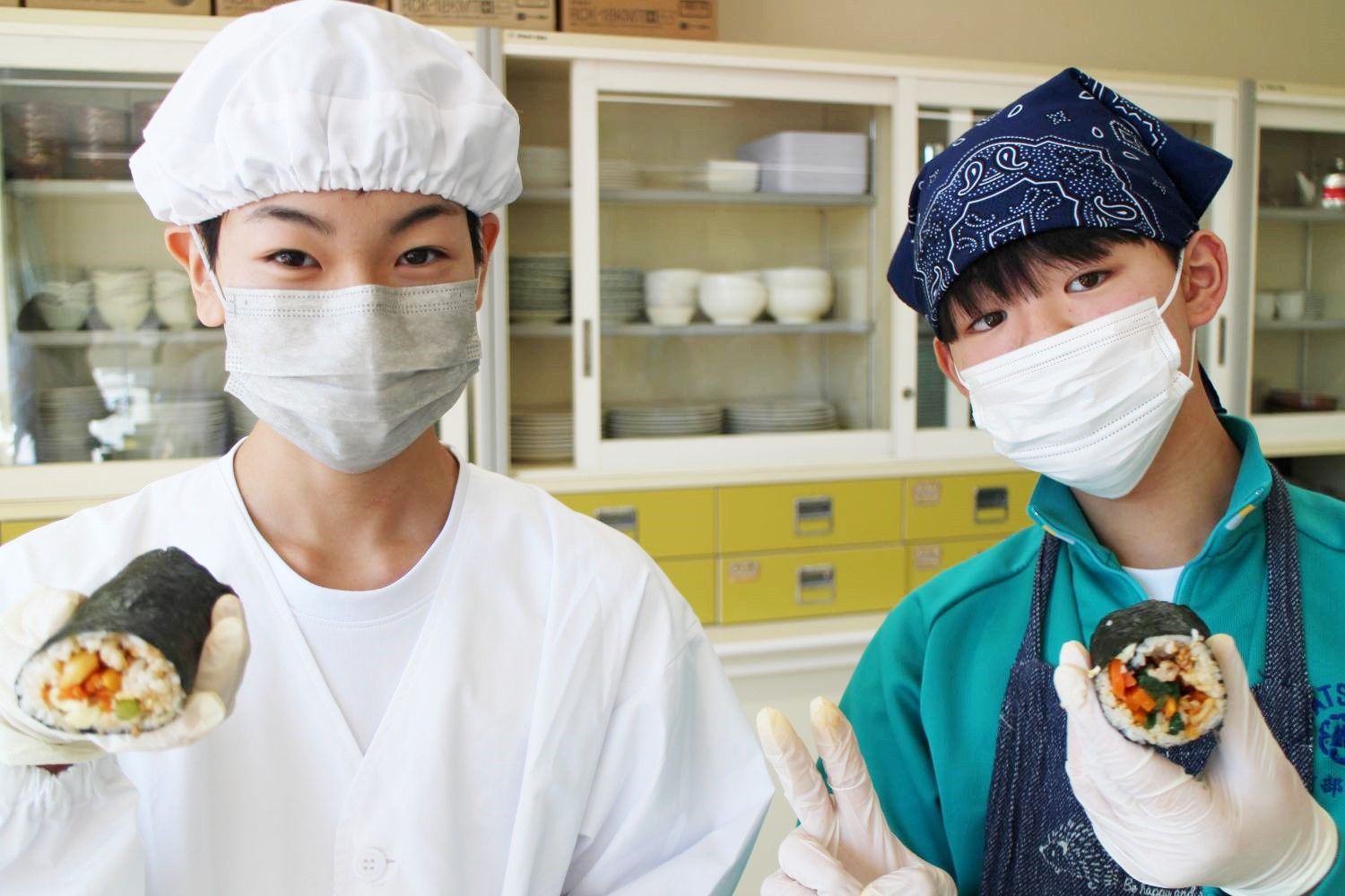 男子生徒2人が、自分たちで作ったキンパを手に持ち、誇らしげにカメラに向かって見せている写真