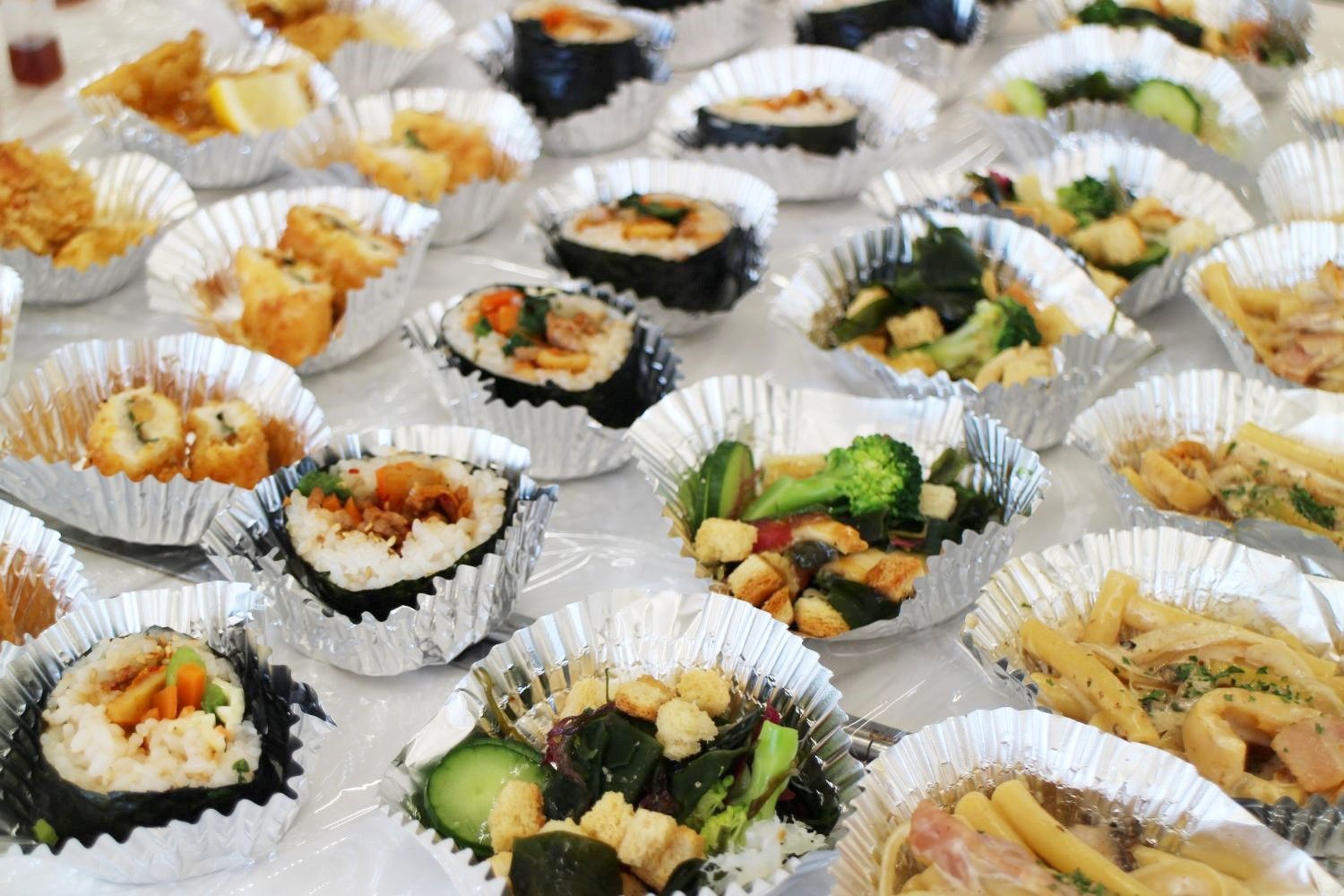 アルミカップに盛りつけられた多種類のホヤ料理がテーブルいっぱいに並べられている様子の写真