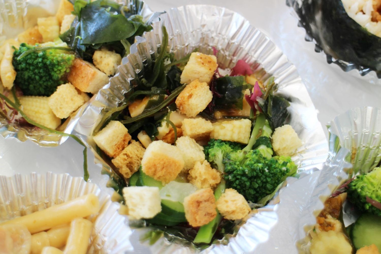 アルミカップの中に、ブロッコリーやヤングコーン、きゅうり、わかめ、クルトンなどが色鮮やかに盛りつけられたサラダの写真