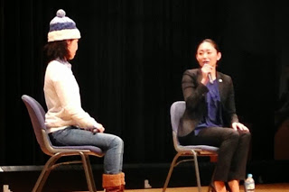 椅子に座った安藤美姫さんがマイクを持ち、隣の女性とトークセッションをしている舞台を写した写真