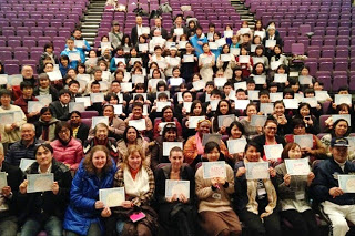 紫色の椅子に座ったたくさんの参加者が胸元に紙を置いてみんなで記念撮影をしている写真