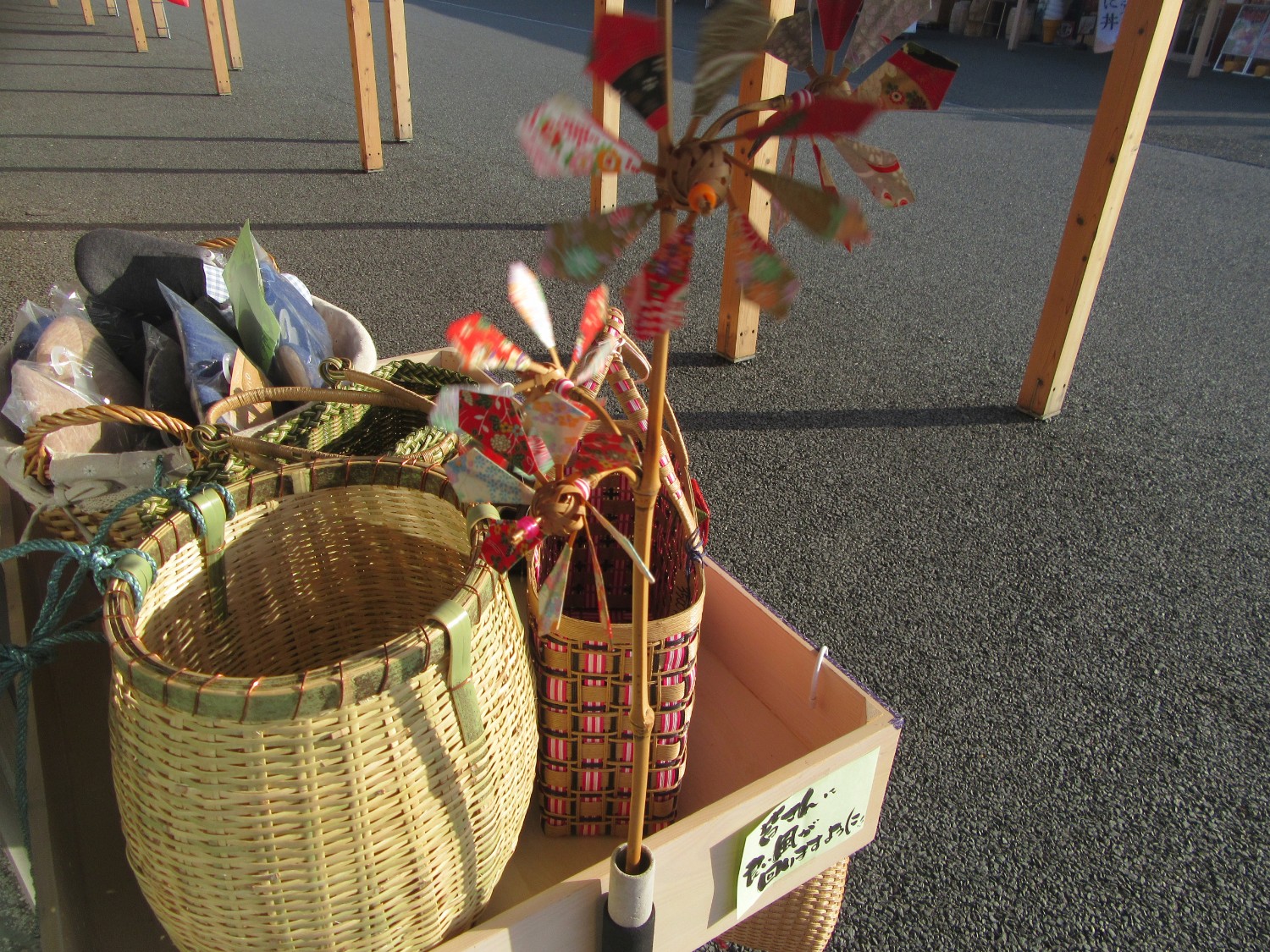 屋外の木製の箱に風車が飾られており、中には数種類の竹かごなどが並んでいる写真