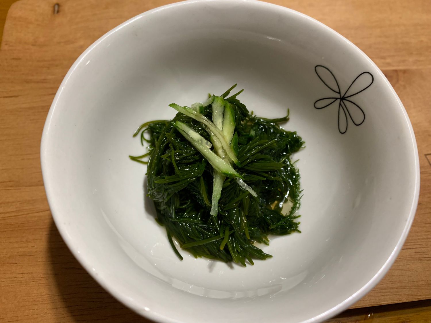 白い器に、上には千切りのきゅうりが添えられた緑色の細い海藻のまつもの酢の物が盛られている写真