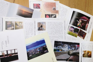 床の上に美しい風景や祭りの写真、文章が散りばめられている冊子のページが何枚も広げられている写真