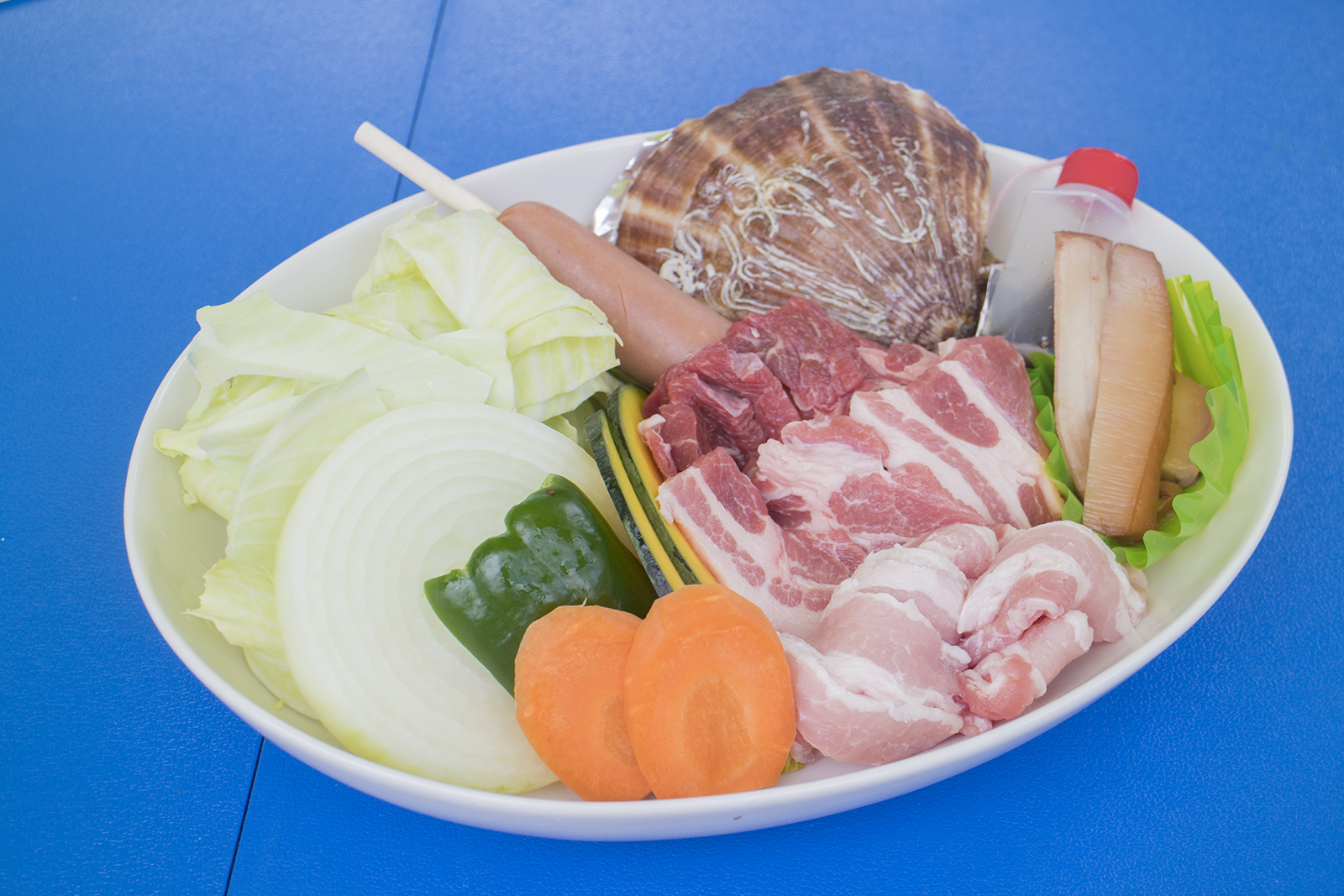 白い深皿にたくさんの野菜、肉、ソーセージ、殻付きのホタテが盛り付けられたバーベキューセットの写真