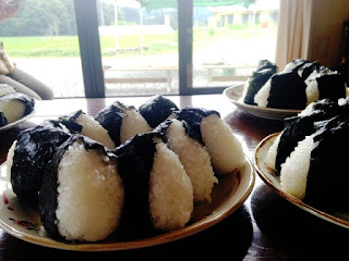 光の入る窓の前のテーブルの上に、海苔で巻かれた三角形の白いおにぎりが多数、皿にきれいに盛り付けられている写真