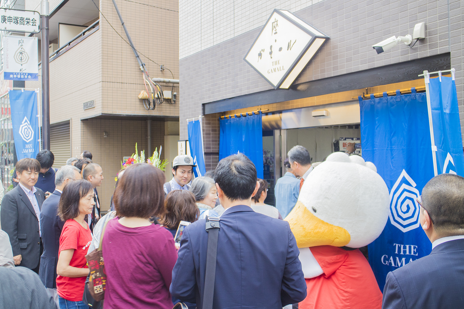 座・ガモールの店舗前に大勢の人が集まっており、すがもんの着ぐるみが出迎えている様子の写真