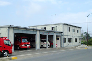 2階建てのプレハブの隣の大きな車庫に救急車と消防車が駐車してあり、手前に1台の消防車が停まっている南三陸消防署の写真