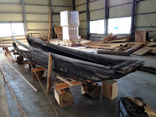台座の上に置かれた長い木製の古い和船が修復のために作業場の中央に設置されている写真