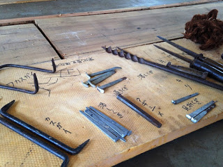 木の板の上に並べられた釘抜き、ノミ、錐などの古い工具に名前が書かれて展示されている写真