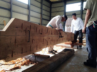 職人が大きな木材に伝統的な工具を使って彫刻しながら合木船の修復作業を進めている様子の写真