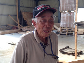 作業場で笑顔を見せて立っている、船大工さんの写真