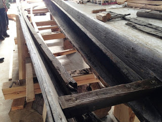 焼け焦げたような色の木材でできた和船の船体部分を間近から見た、損傷の状態がわかる修復中の写真