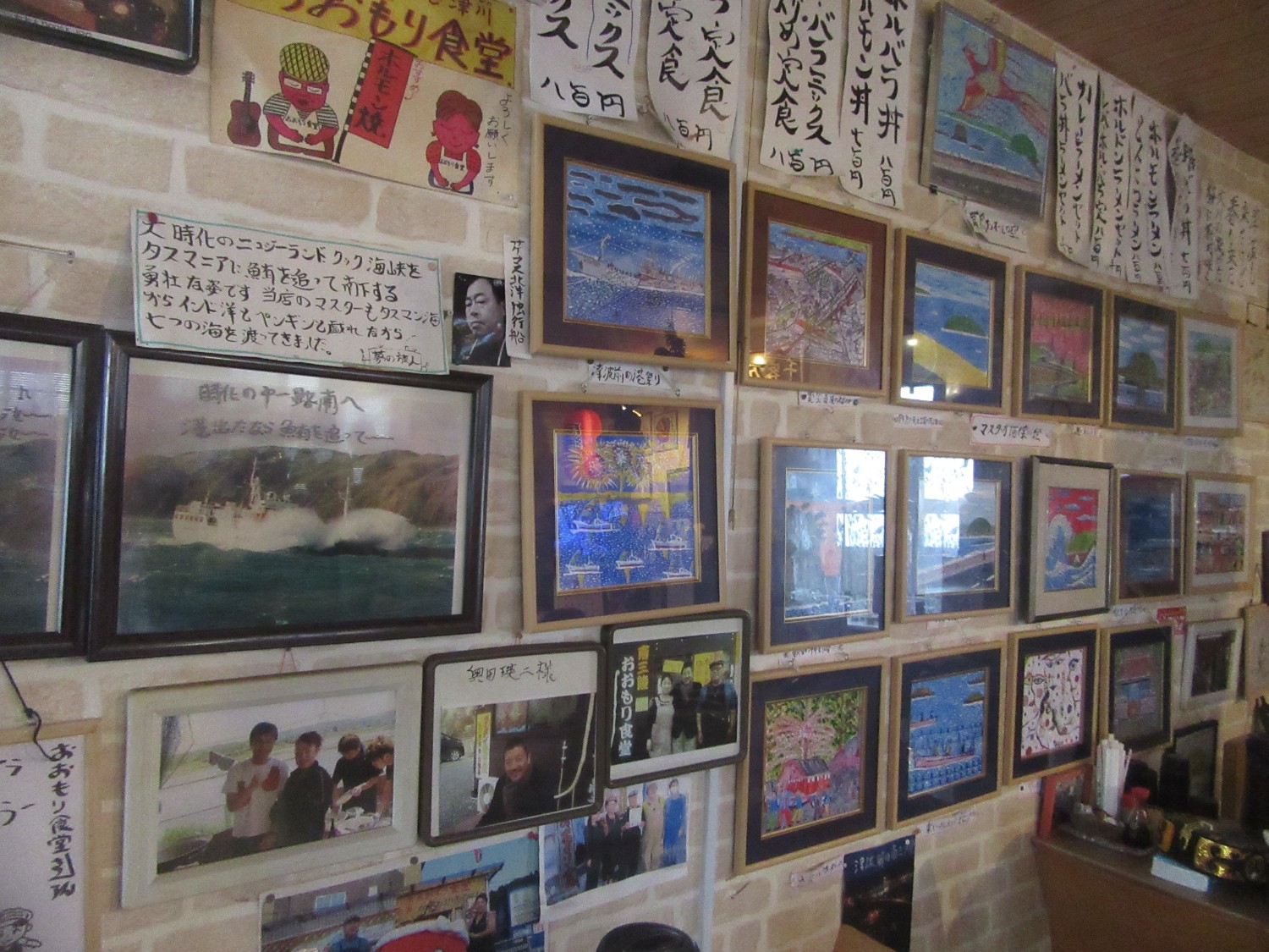壁一面に色とりどりの絵や写真、手書きのメニューなどが丁寧に飾られている店内の写真