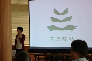 スライドに「南三陸杉」の文字と翼のような羽の形が縦に3つ並んだようなロゴが映されていて、講演者が説明している講演会の様子の写真