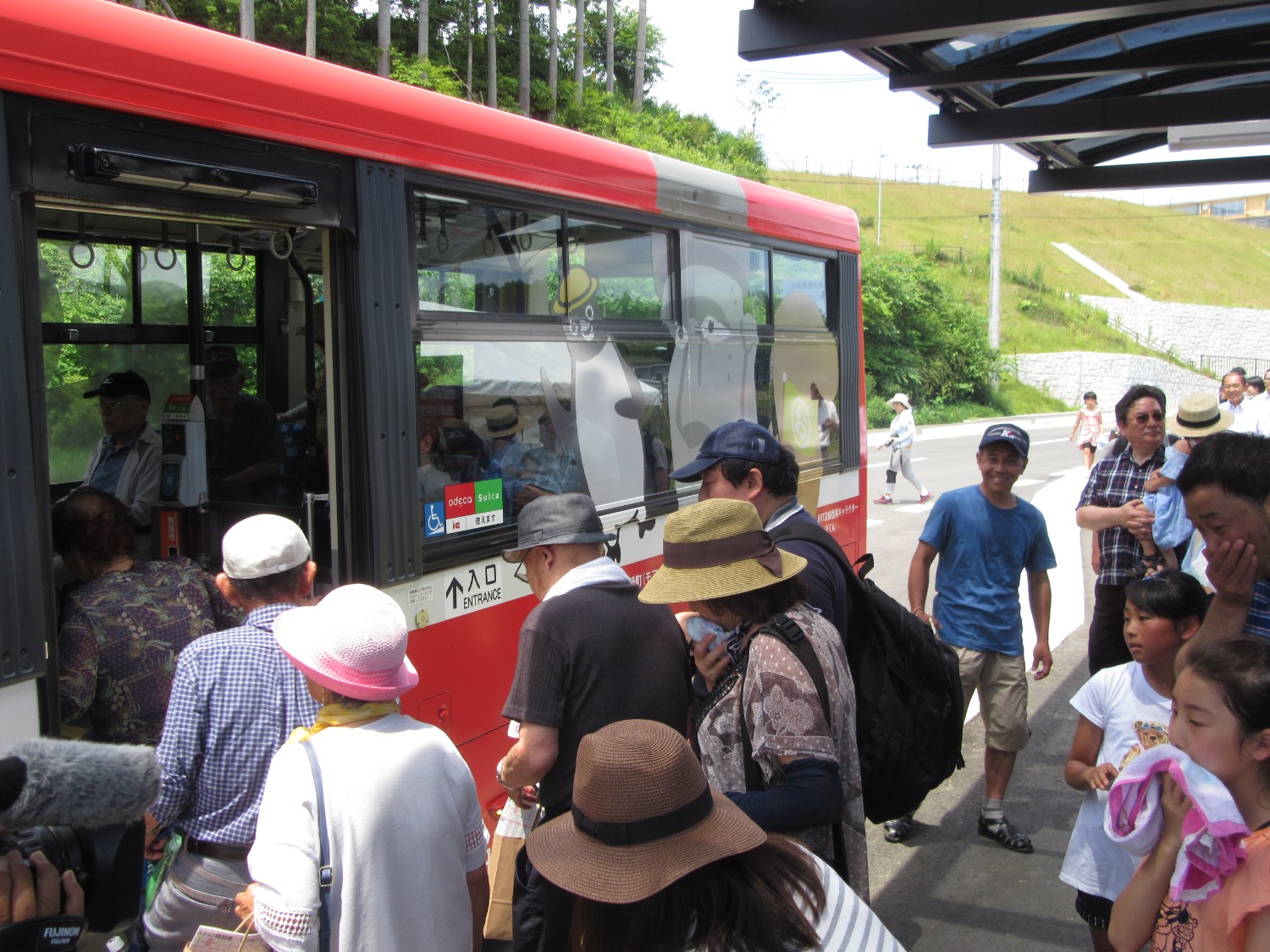 赤と白のバスの側面に「入口」と表示された乗降口に、多くの人が乗り込もうとしている様子の写真