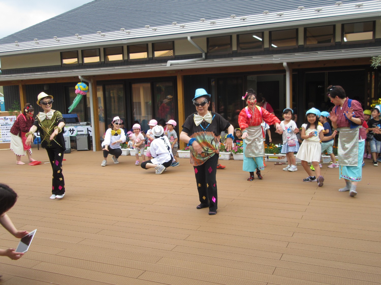 色とりどりの仮装をした大人たちと園児がダンスを披露している様子の写真