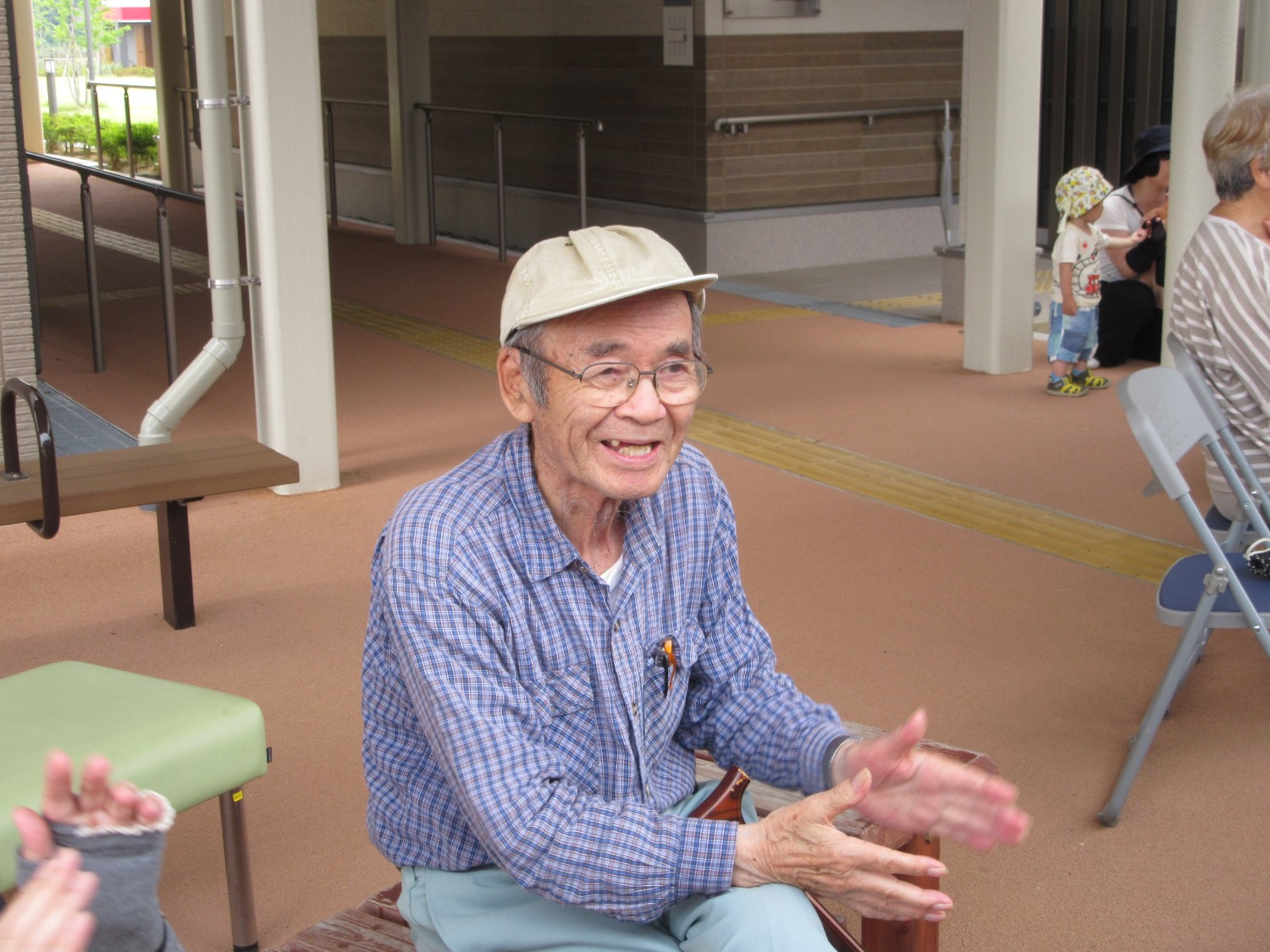 帽子をかぶり眼鏡をかけた山内さんがベンチに座りながら笑顔で拍手をしている写真