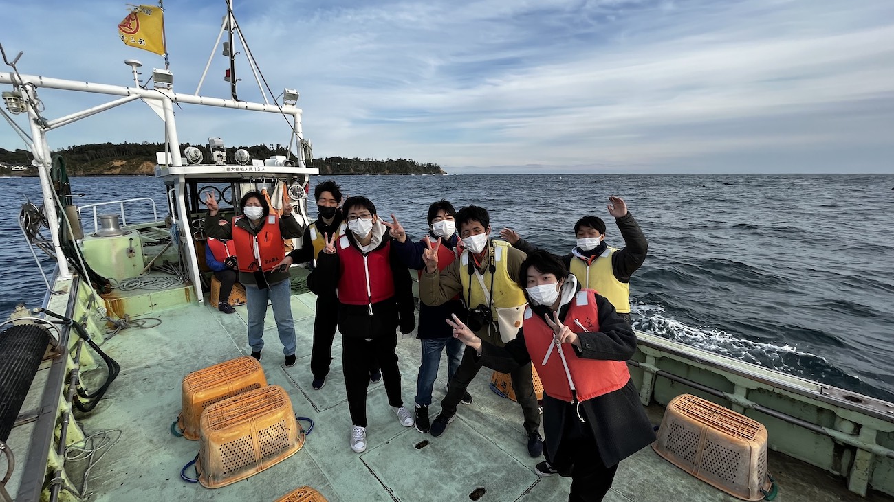 学生たちがライフジャケットを着用して漁船に乗り込み、海上で漁業体験をしている様子の写真