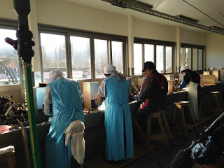 光の差し込む作業場で数人の女性が腰掛けて並び、牡蠣の殻を剥く作業をしている写真